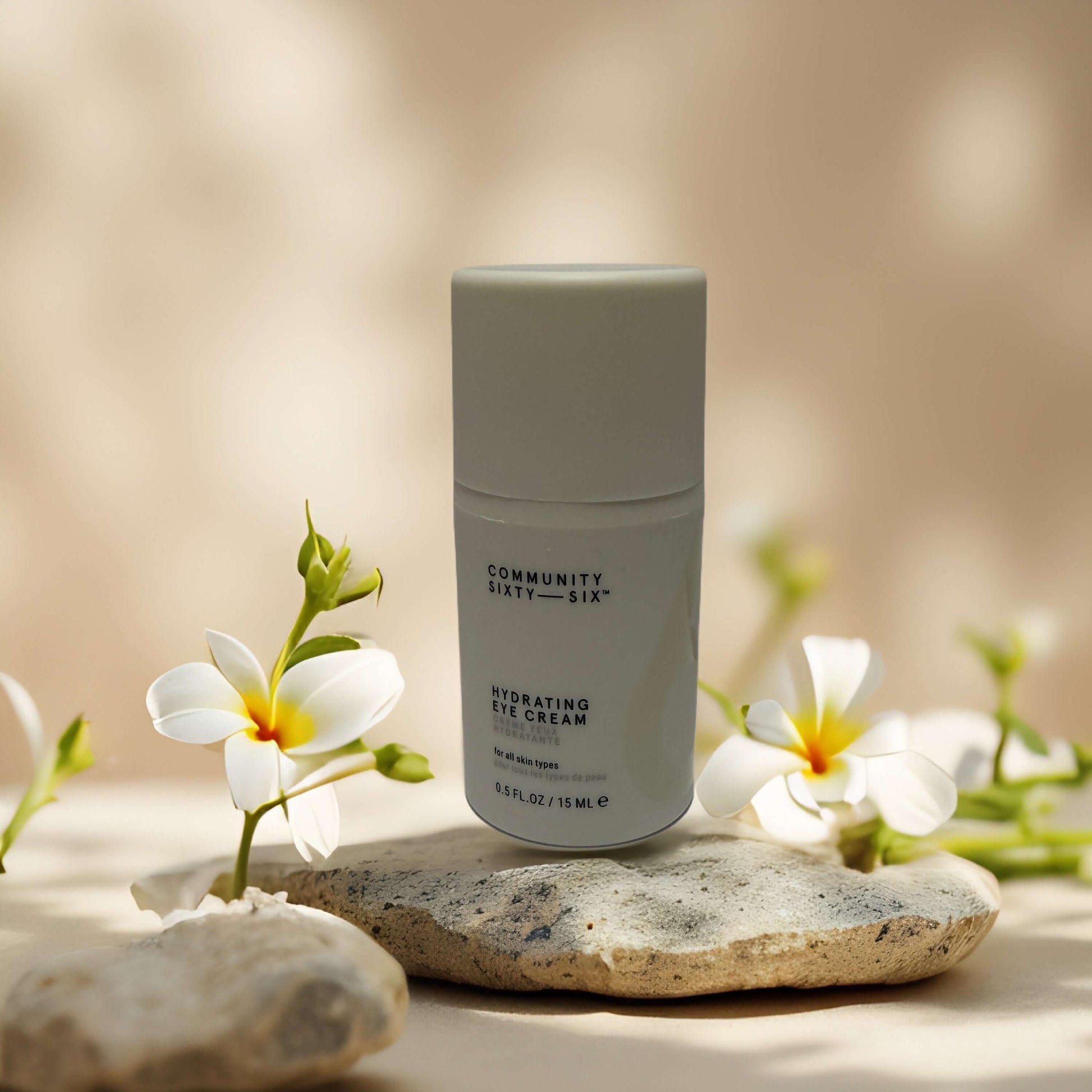 Bright-Eyed Boost Hydrating Eye Cream by Community Sixty-Six on a stone, surrounded by flowers.