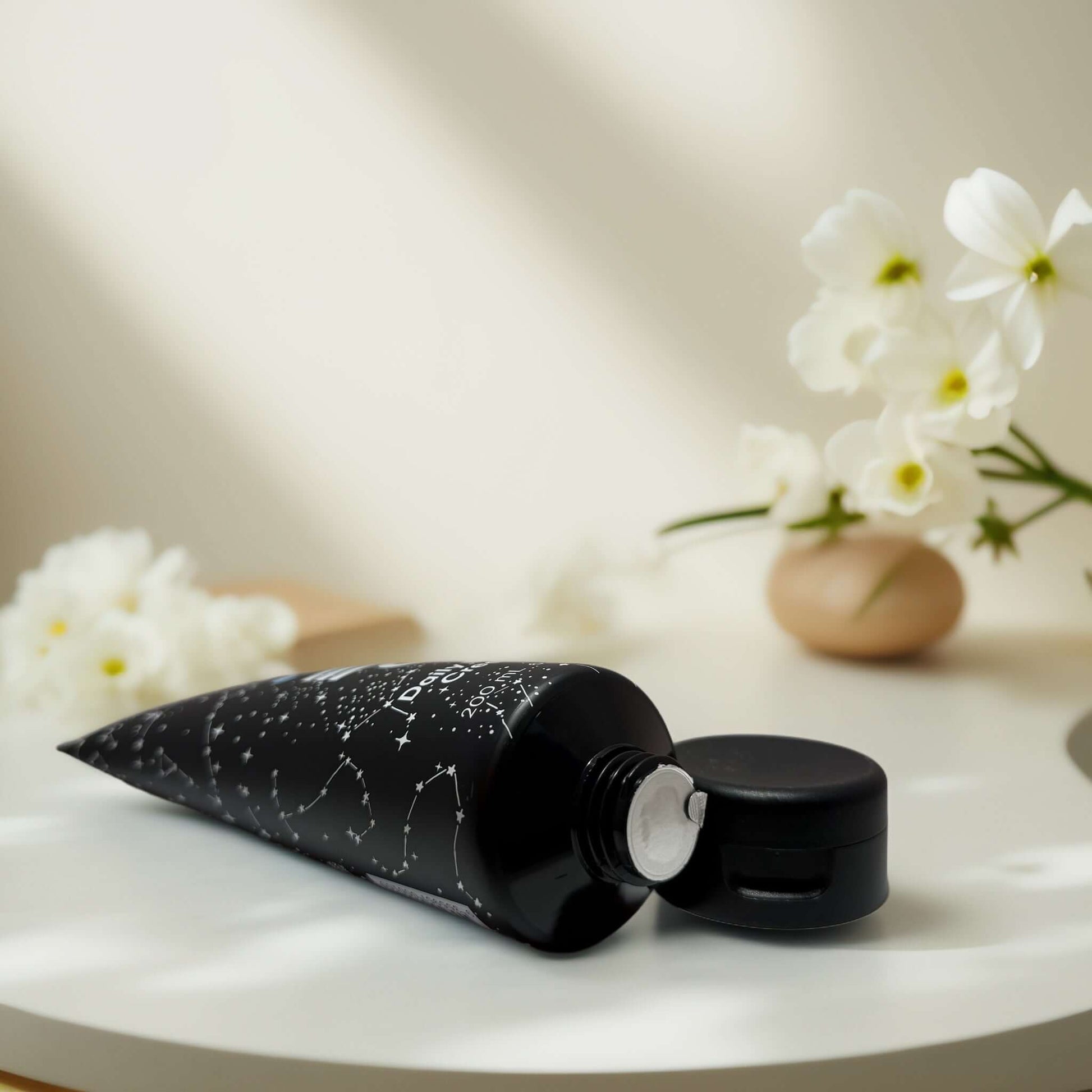 Hydration Boost Daily Body Cream tube on a table with flowers.