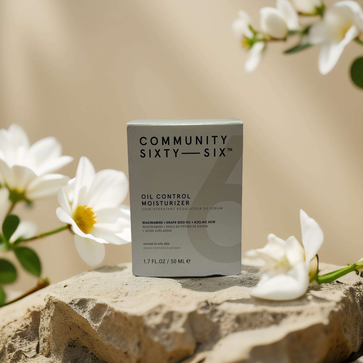 Community Sixty-Six Oil Control Moisturizer in packaging, surrounded by flowers on a stone surface.