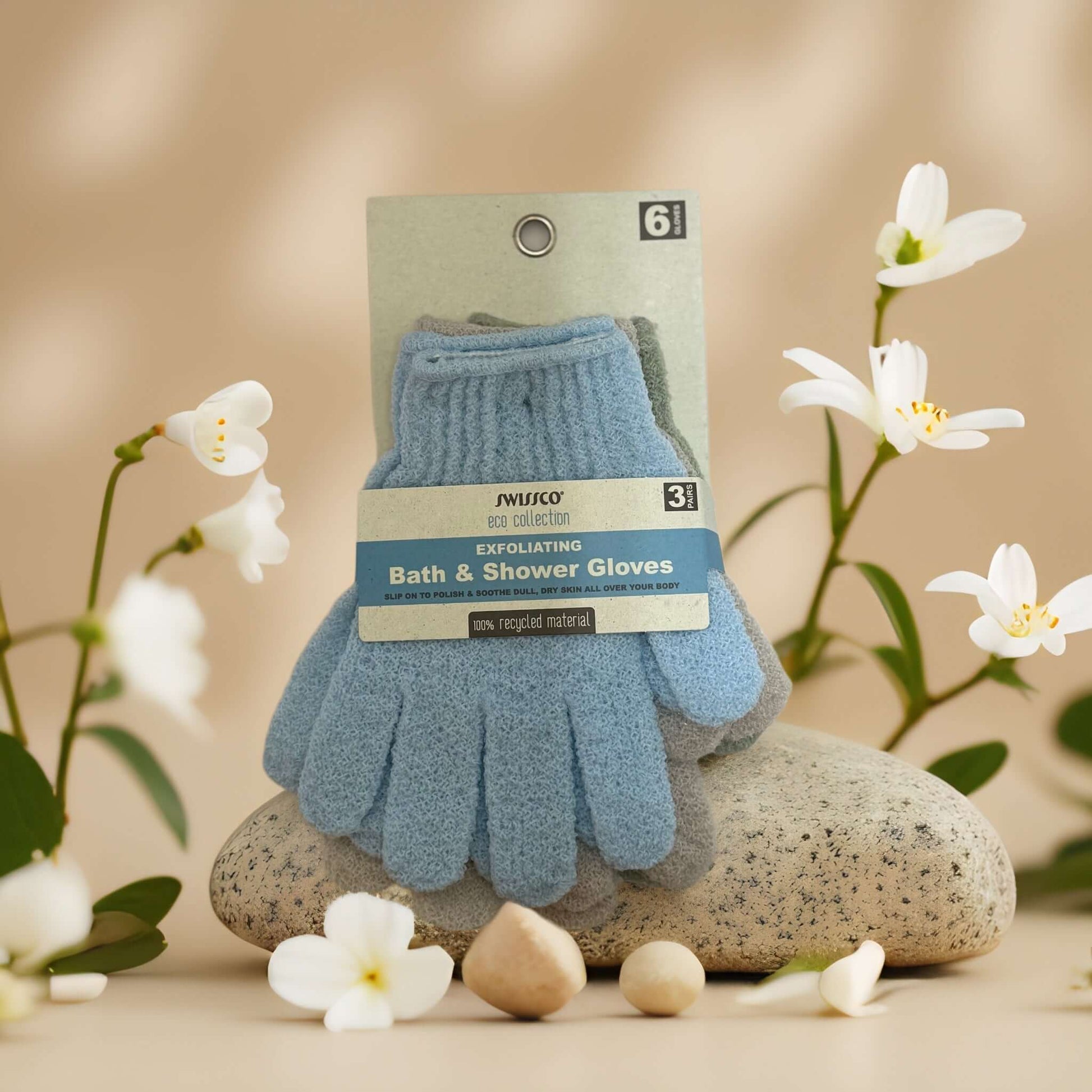 Exfoliating bath and shower gloves in blue packaging, surrounded by flowers and stones for spa-like relaxation.